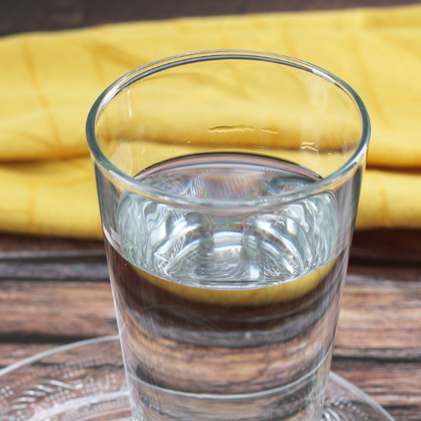 Glas Wasser mit gelbem Hintergrund und Serviette – neutrale Produktdarstellung des Trinkglases