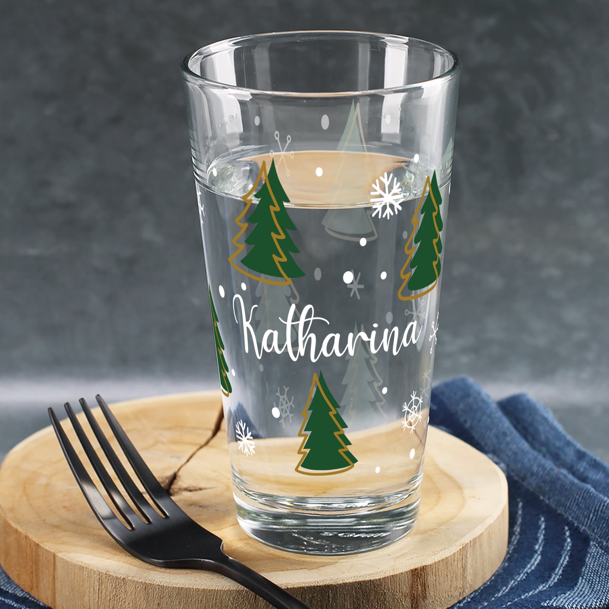 Personalisierbares Trinkglas mit Weihnachtsbaum-Motiv und Schneeflocken – bedruckt mit individuellem Namen, weihnachtlich dekoriert.