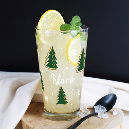 Personalisierbares Weihnachtsglas mit Tannenbäumen, Schneeflocken und Namen – auf rustikaler Holzscheibe arrangiert.