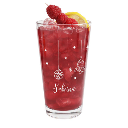 Festliches Glas mit weißen Weihnachtskugel- und Glockenmotiven, befüllt mit rotem Getränk und Eis, dekoriert mit Zitronenscheibe und Himbeeren.