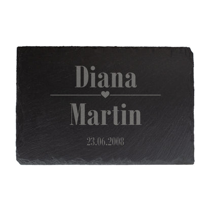 Schieferplatte als Beispielgravur mit Platzhaltern „Name 1, Name 2“ und „Datum“, mittig ein kleines Herzsymbol, auf weißem Hintergrund
