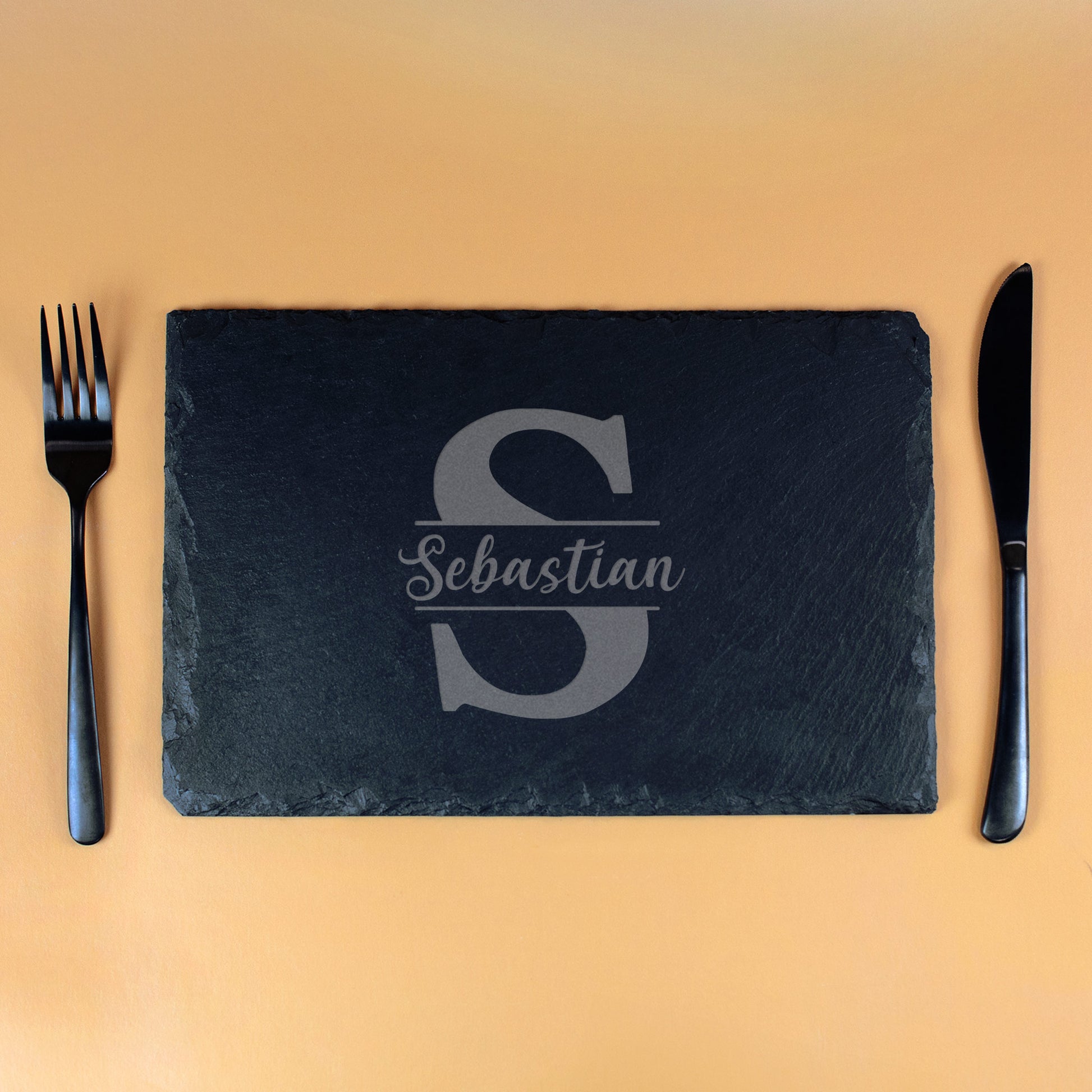 Personalisierte Schieferplatte mit Gravur „S“ und Name Sebastian, rechteckige Platte mit schwarzem Besteck auf orangem Hintergrund