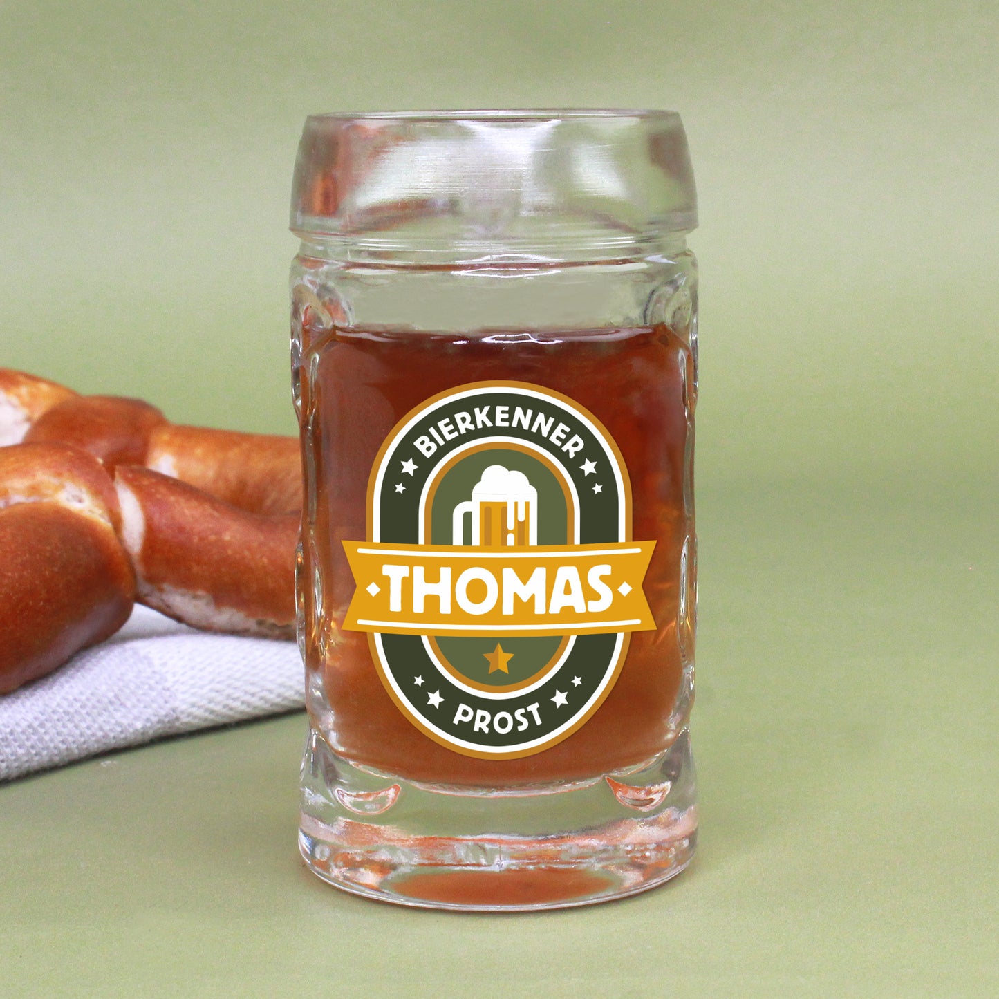 Mini-Bierkrug mit 4 cl Fassungsvermögen, frontal fotografiert, mit Bierkenner-Motiv und personalisiertem Namen „Thomas“, im Hintergrund Brezeln auf einem Tuch – ideal als witziges Schnapsglas mit bayerischem Flair