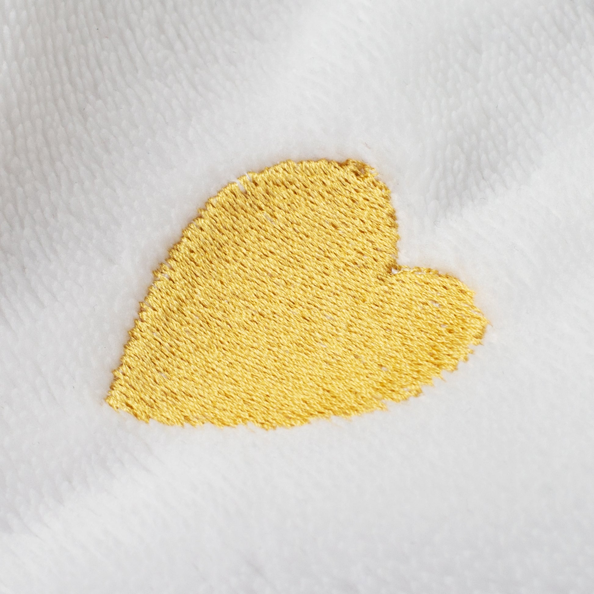 Nahaufnahme goldenes Herz als Stickerei auf weißem Bademantel, strukturierte Frottee-Oberfläche