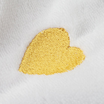 Nahaufnahme goldenes Herz als Stickerei auf weißem Bademantel, strukturierte Frottee-Oberfläche