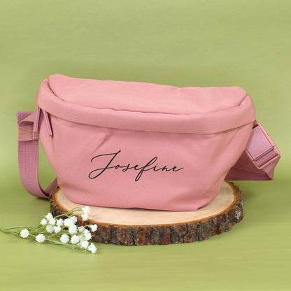 Rosa Bauchtasche mit Name Josefine auf Holzscheibe, dekoriert mit kleinen weißen Blüten