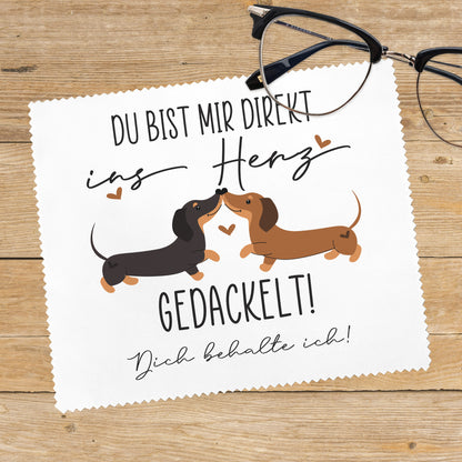 Dackel-Brillenputztuch auf Holzuntergrund mit Brille, Motiv „Du bist mir direkt ins Herz gedackelt!“, Wunschtext „Dich behalte ich!“