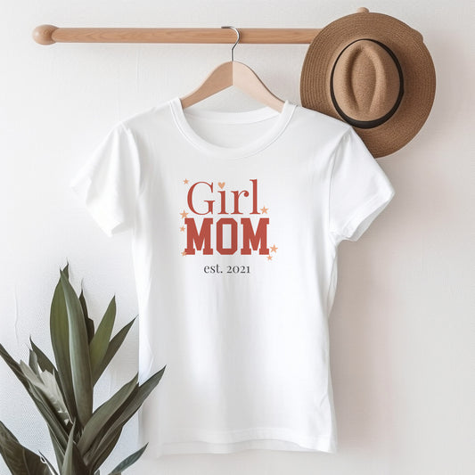 Damen T-Shirt „Girl Mom“ auf Kleiderbügel mit Hut im Hintergrund, personalisiert mit Jahreszahl