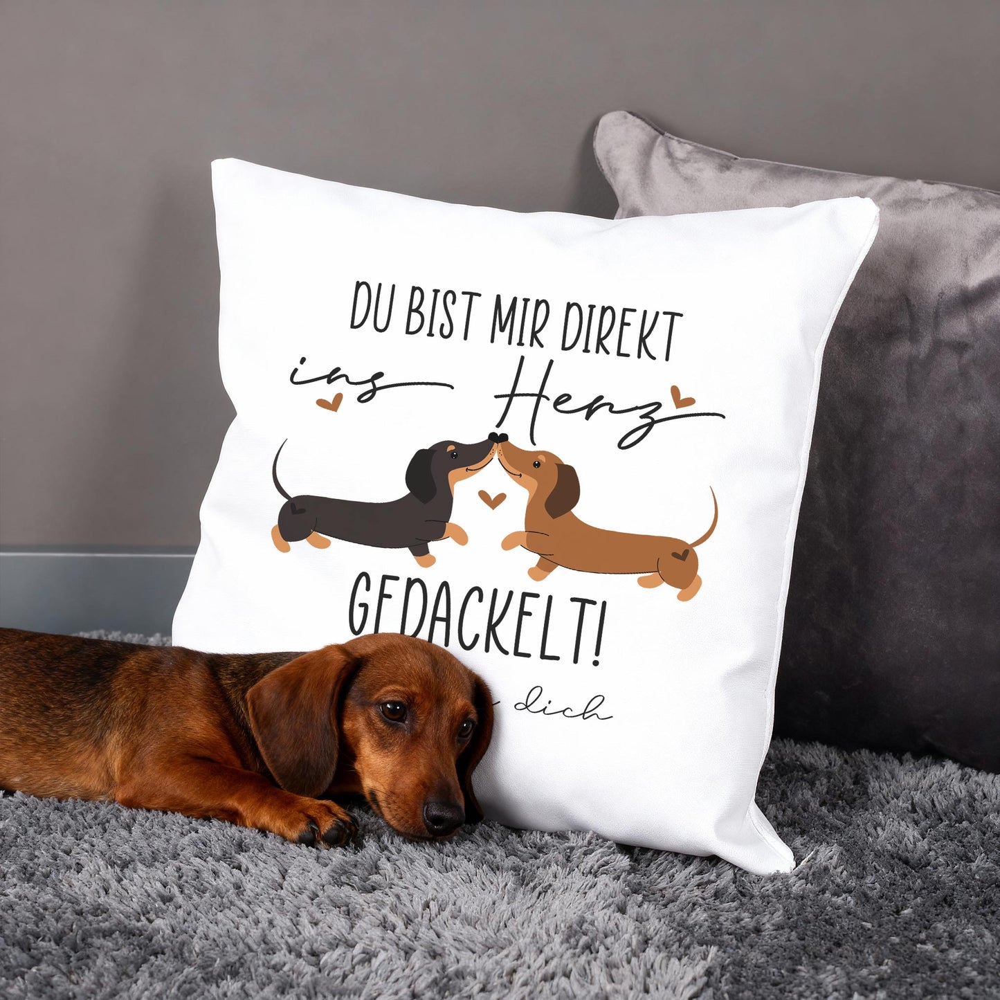 Personalisiertes Kissen mit Dackel-Pärchen und Spruch „Du bist mir direkt ins Herz gedackelt!“, Hund liegt davor