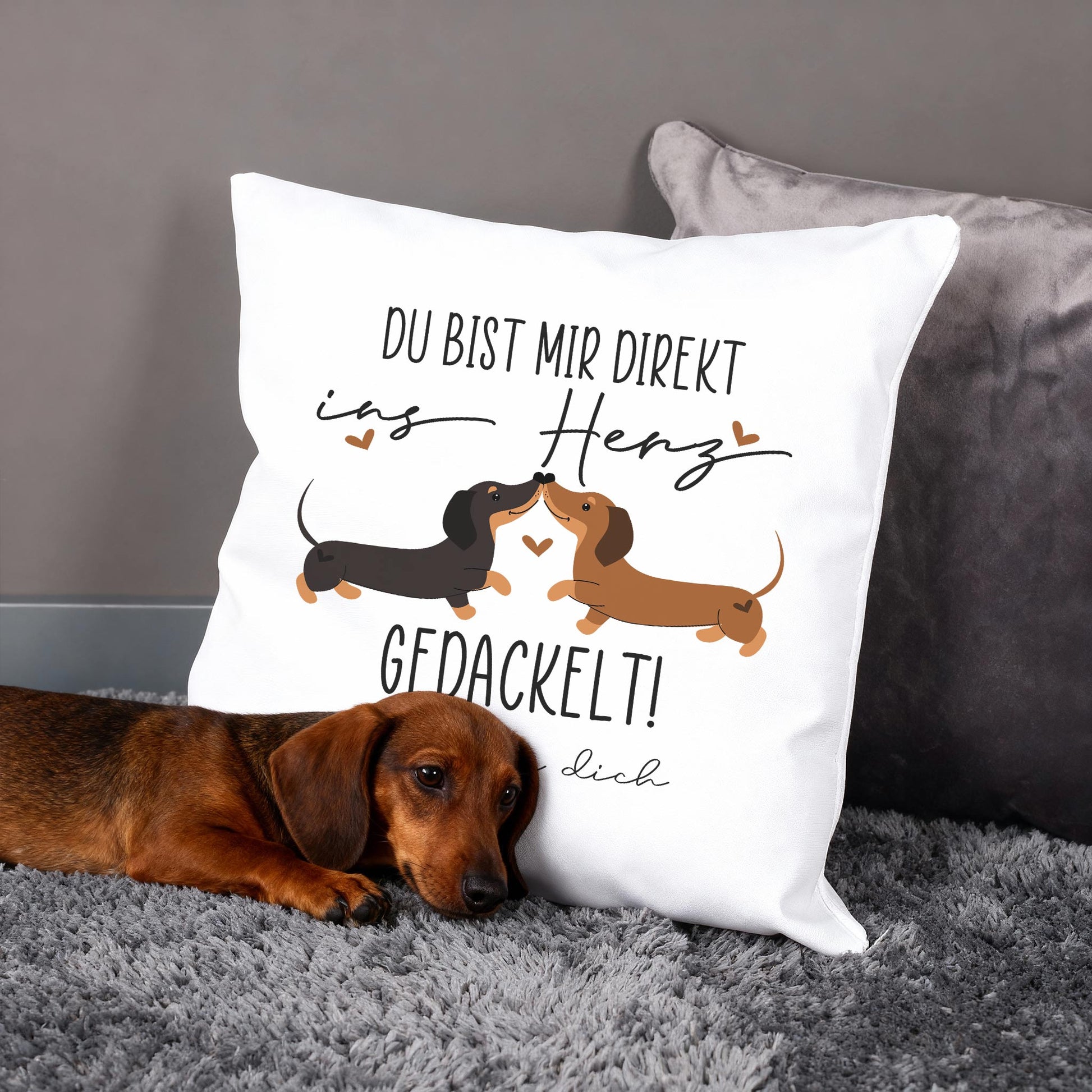 Personalisiertes Kissen mit Dackel-Pärchen und Spruch „Du bist mir direkt ins Herz gedackelt!“, Hund liegt davor