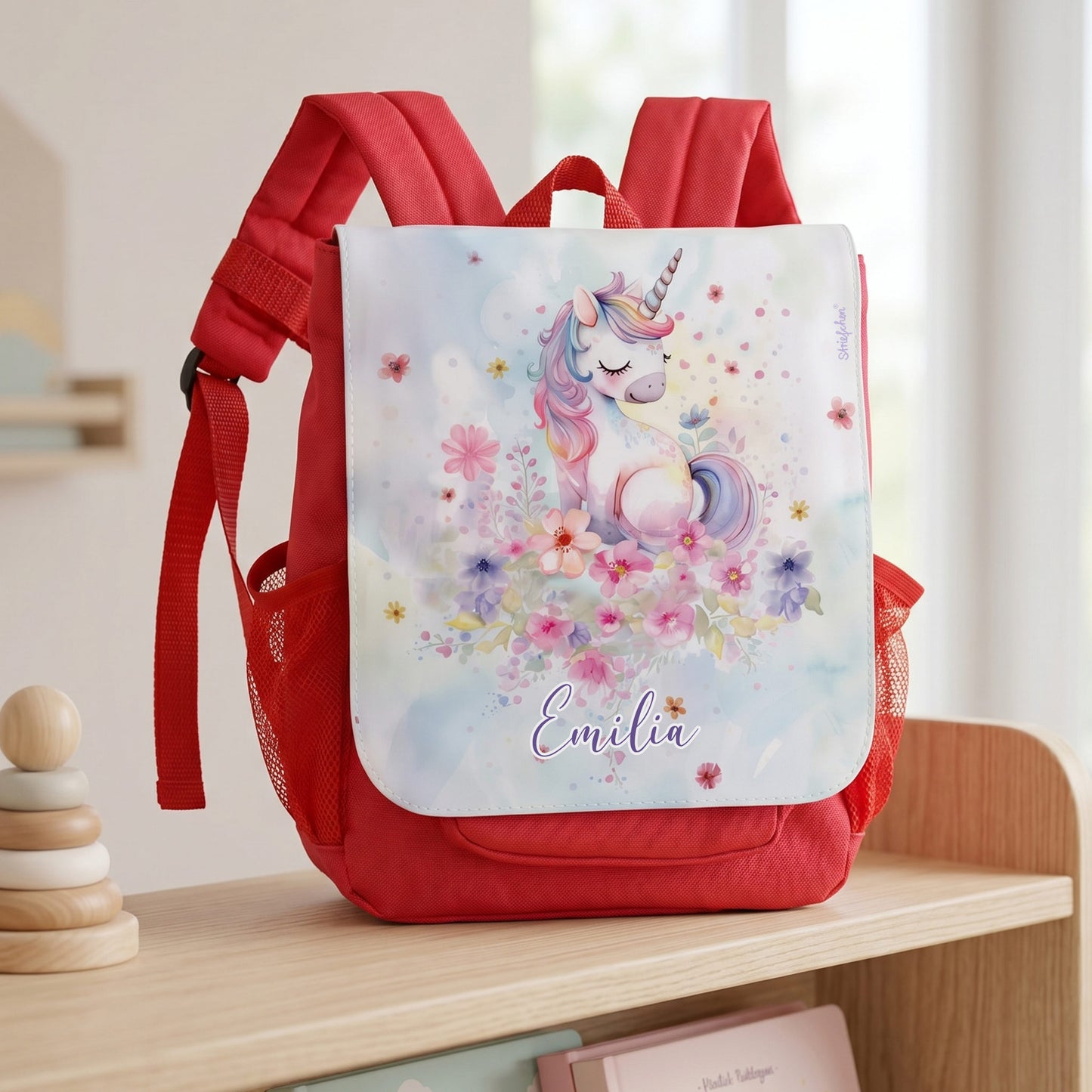 Personalisierter Kinder Rucksack in Rot mit Einhorn, Blumenmotiv und Name Emilia auf heller Holzbank