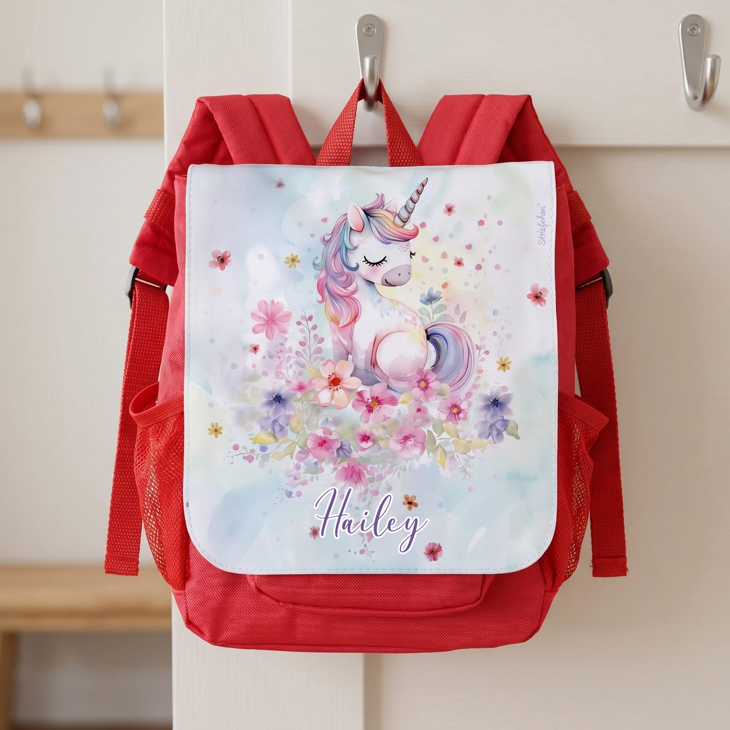 Roter Kita Rucksack mit abnehmbarer Frontlasche, Einhornmotiv und Name Hailey an einer Garderobe