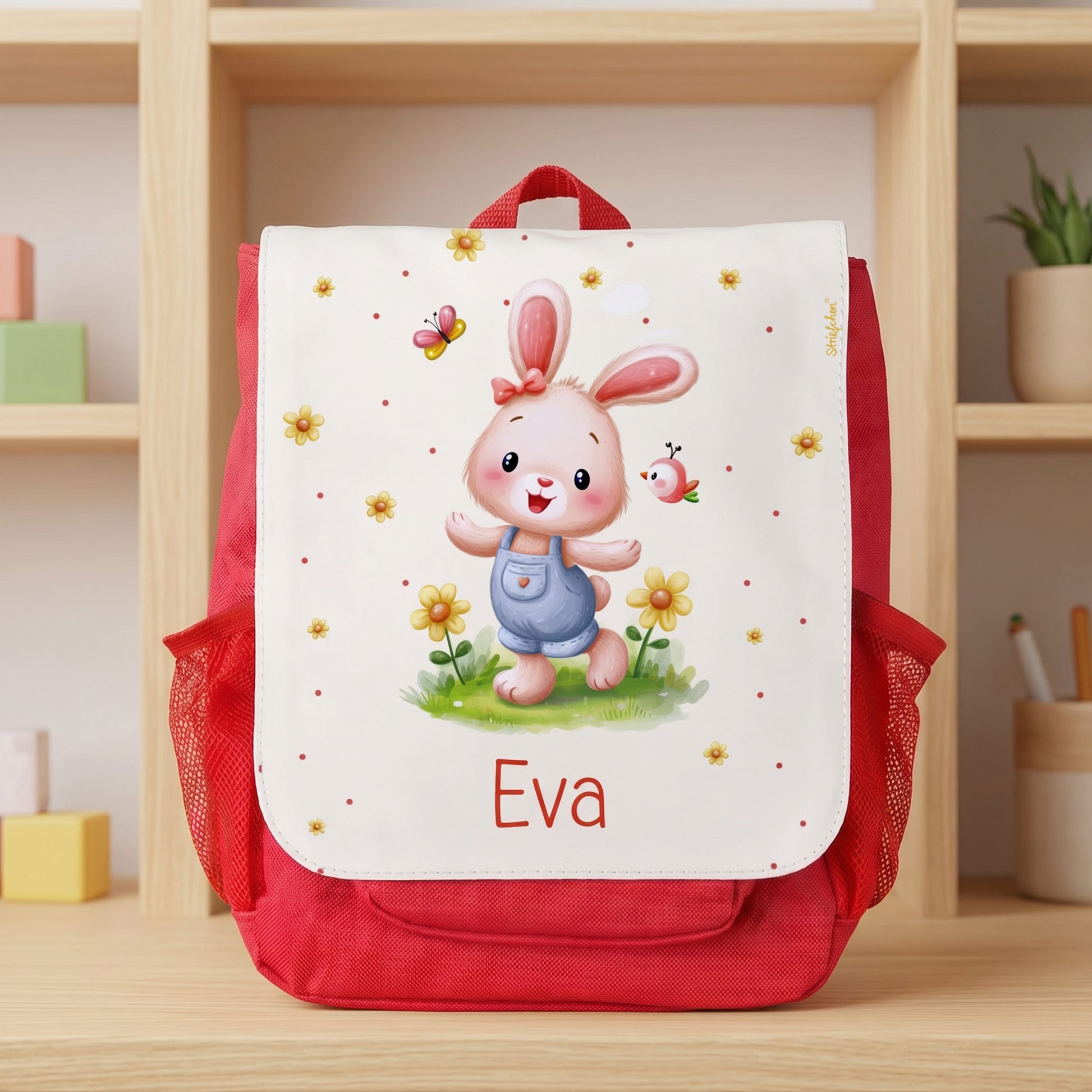 Roter Kinderrucksack mit süßem Hase, Blume, Schmetterling und Name Eva auf hellem Regal