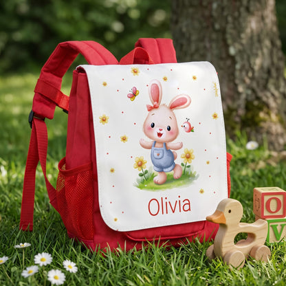 Roter Kinderrucksack mit niedlichem Hase, Blumen, Holzspielzeug und Name Olivia im Gras