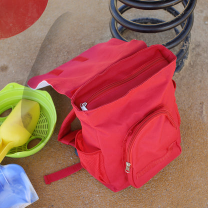 Geöffneter roter Kinder Rucksack mit Hauptfach, Reißverschlüssen und seitlichem Netzfach auf dem Spielplatz