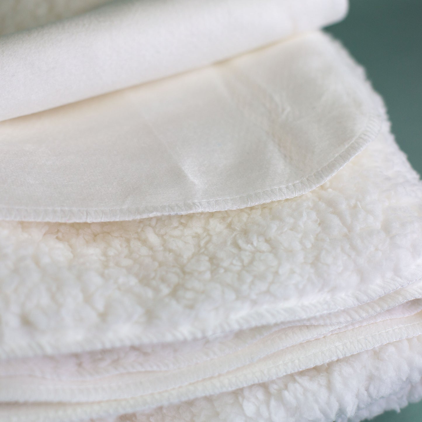 Detailaufnahme Kuscheldecke mit weicher Sherpa-Rückseite und flauschiger Struktur, Materialansicht der Decke