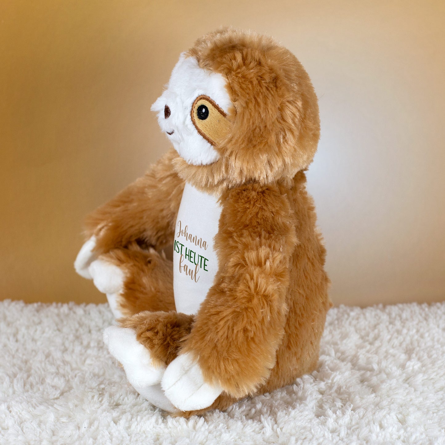 Seitliche Ansicht des Kuscheltiers Faultier mit Aufdruck „Johanna ist heute faul“ auf beigem Hintergrund.