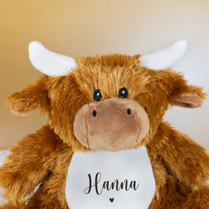 Nahaufnahme des Kuh-Kopfes mit braunem Fell, weißen Hörnern und aufgedrucktem Namen über Herzmotiv.