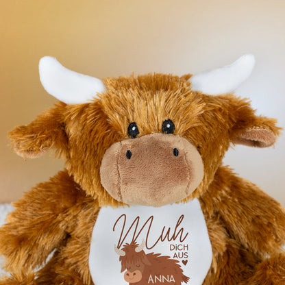 Nahaufnahme des Gesichts der Kuscheltier-Kuh mit weißen Hörnern, braunem Fell und sichtbarem Aufdruck „Muh dich aus“ mit Name Anna auf dem Bauch.
