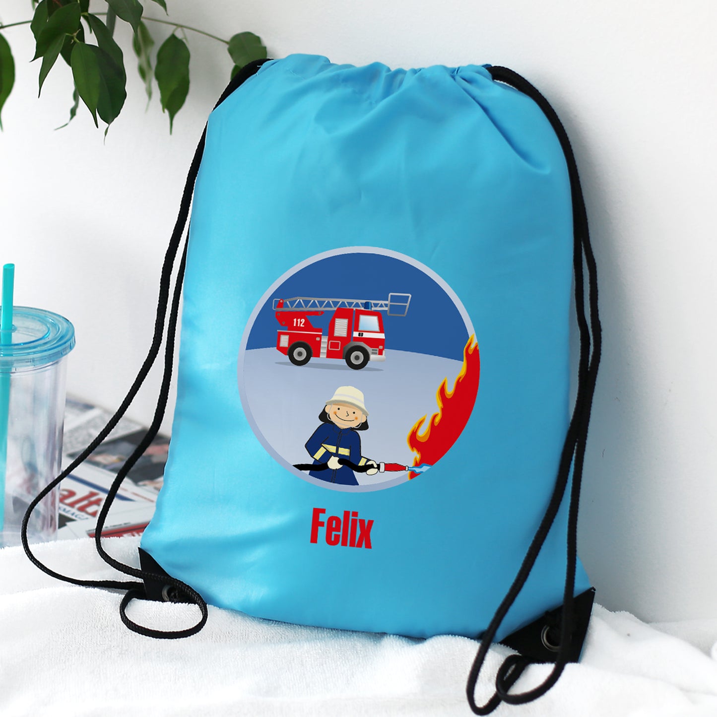 Hellblauer Turnbeutel mit Feuerwehr-Motiv und Wunschname „Felix“, auf einem Stuhl platziert