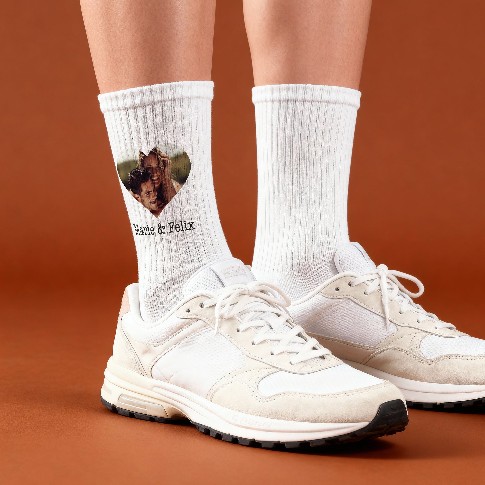 Personalisierte Foto-Socken mit Herzfoto und Wunschtext, getragen am Fuß vor orangem Hintergrund