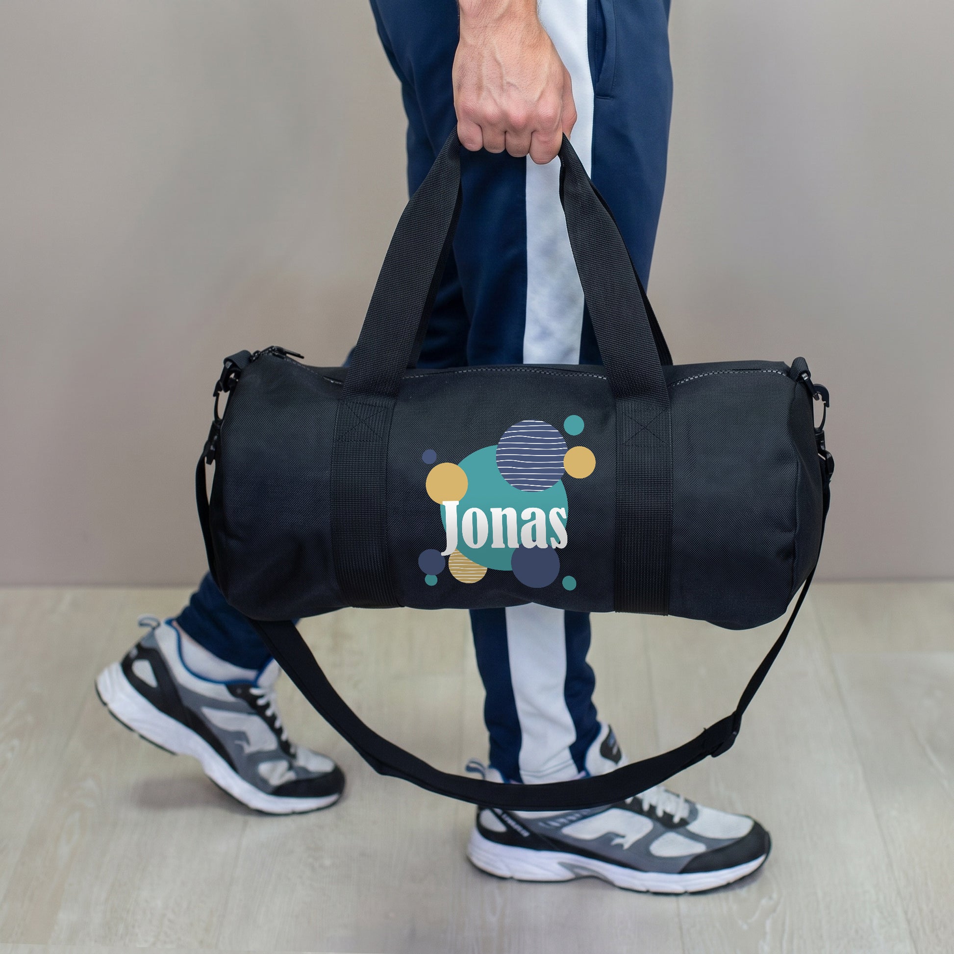 Person trägt schwarze Sporttasche mit Muster-Motiv und personalisiertem Namen Jonas am Tragegriff