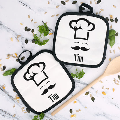 Personalisierbare Topflappen im 2er-Set mit Schlaufe zum Aufhängen auf heller Küchenfläche