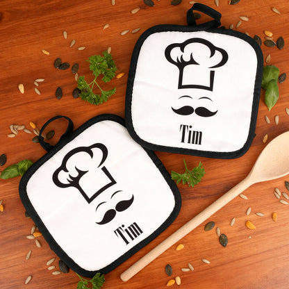 Zwei personalisierte Topflappen mit Koch-Design auf Holzuntergrund mit Kochlöffel dekoriert