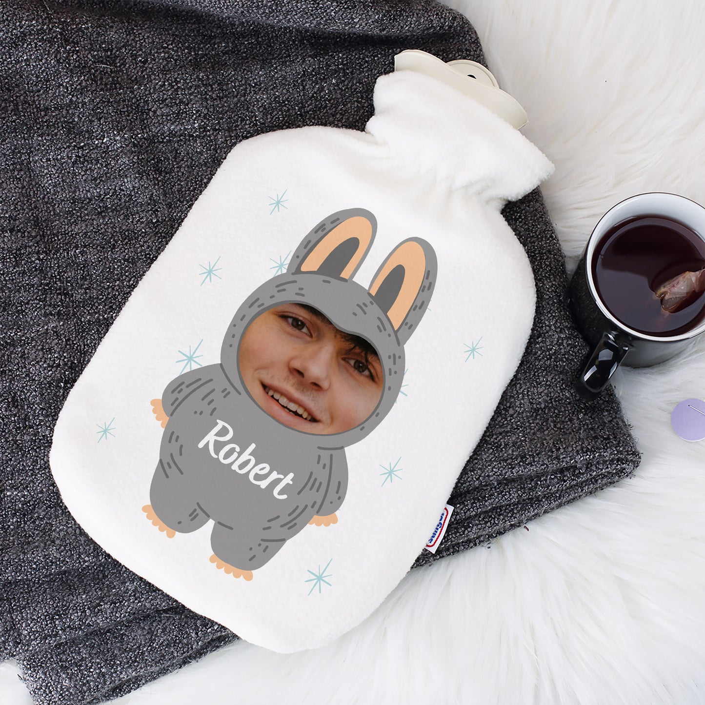 Personalisierte Wärmflasche mit Monster-Motiv, Foto und Name „Robert“ auf weißem Bezug, dekoriert mit Decke und Tee