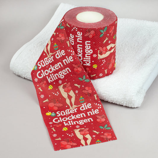 Rote Toilettenpapierrolle mit Weihnachtsmotiv und Spruch „Süßer die Glocken nie klingen“ auf weißem Handtuch