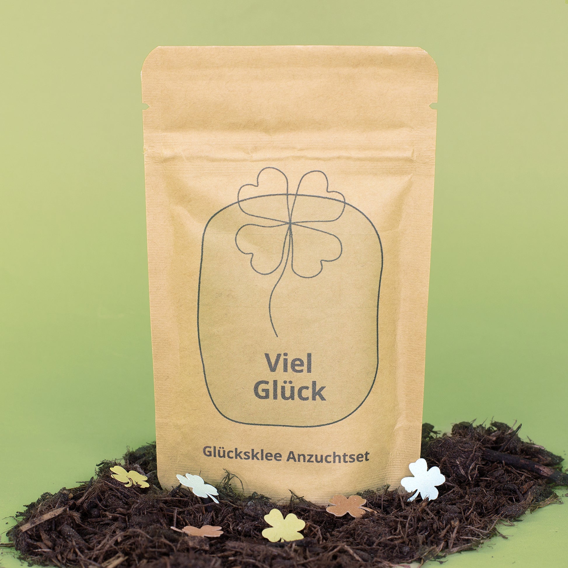 Viel Glück Anzuchtset in brauner Kraftpapiertüte mit Kleeblatt-Motiv zwischen Erde und Streudeko